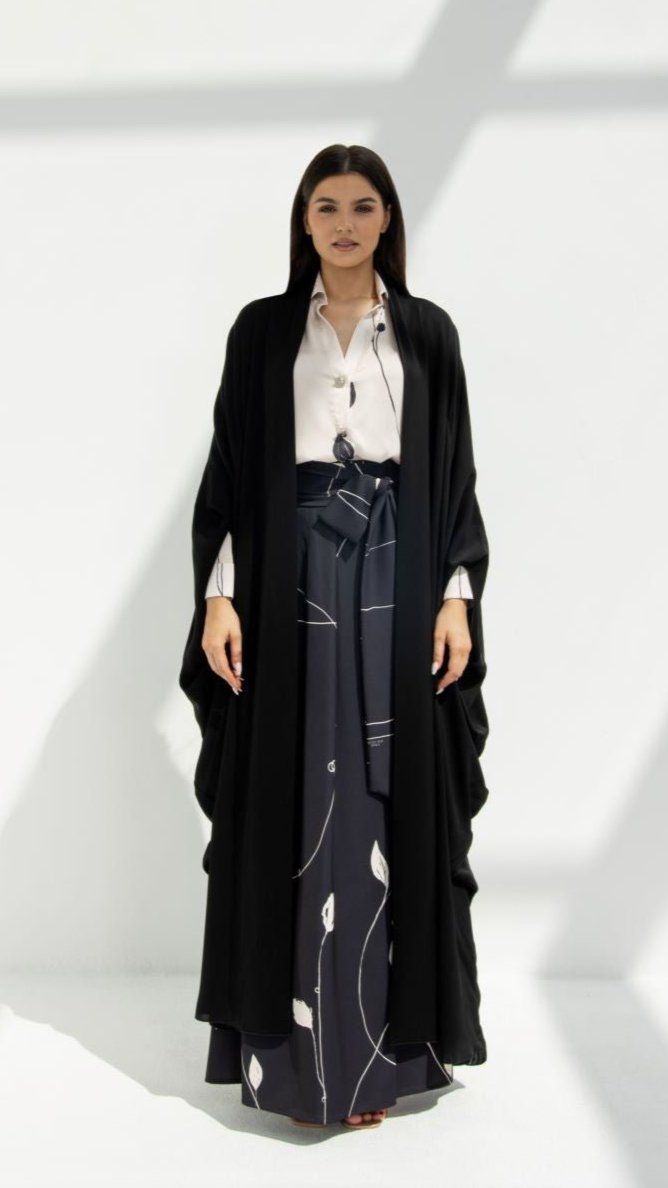 Woman wearing a black luxury Al Zain Abaya over white blouse and patterned navy skirt