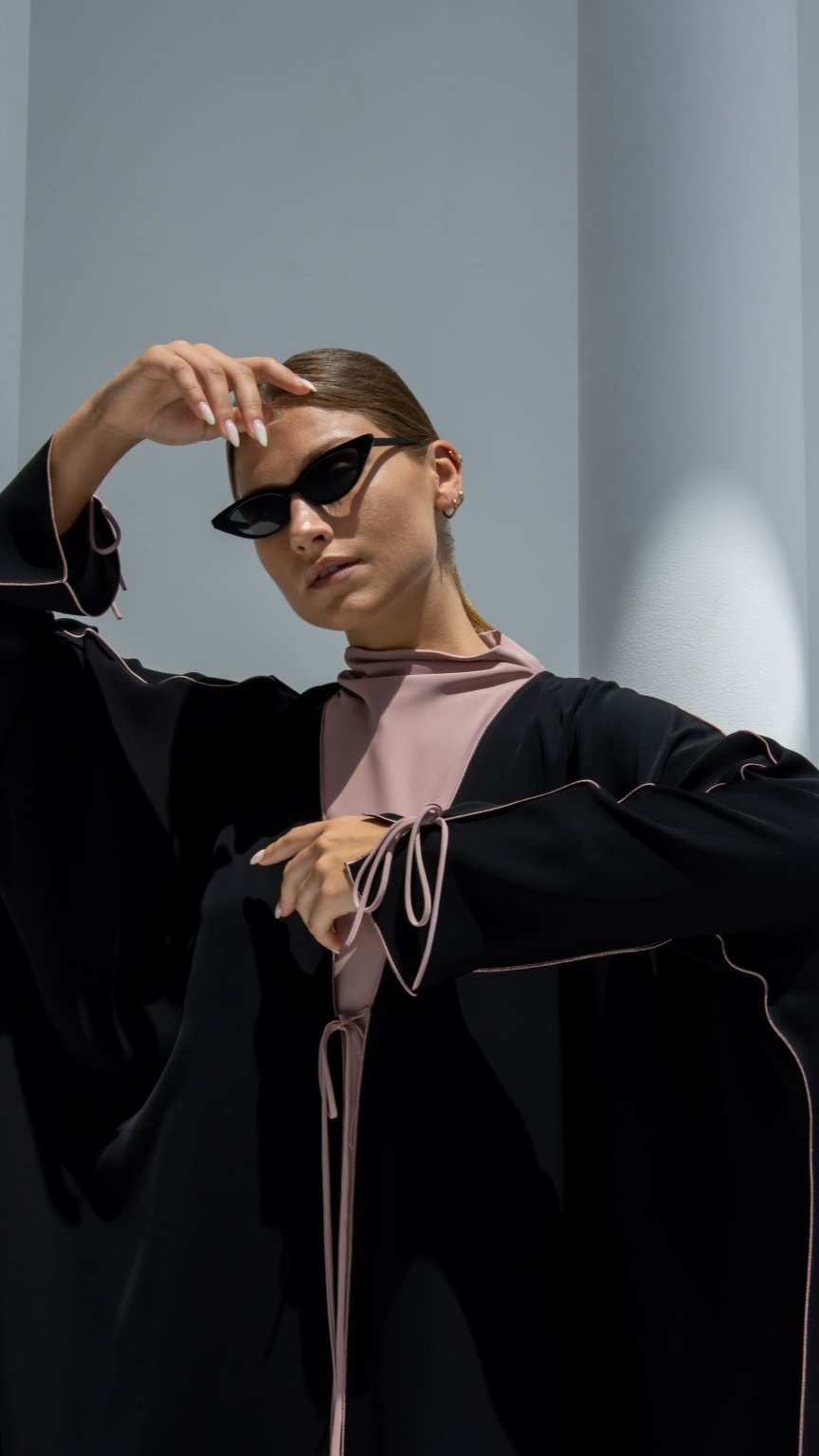 Elegant Bahraini ribbon abaya in black with pink accents, stylishly paired with cat-eye sunglasses