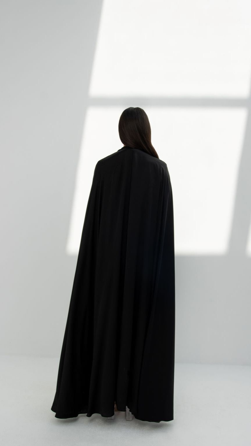 Woman wearing a black elegant abaya designs by Selected Lines seen from the back in minimal studio lighting