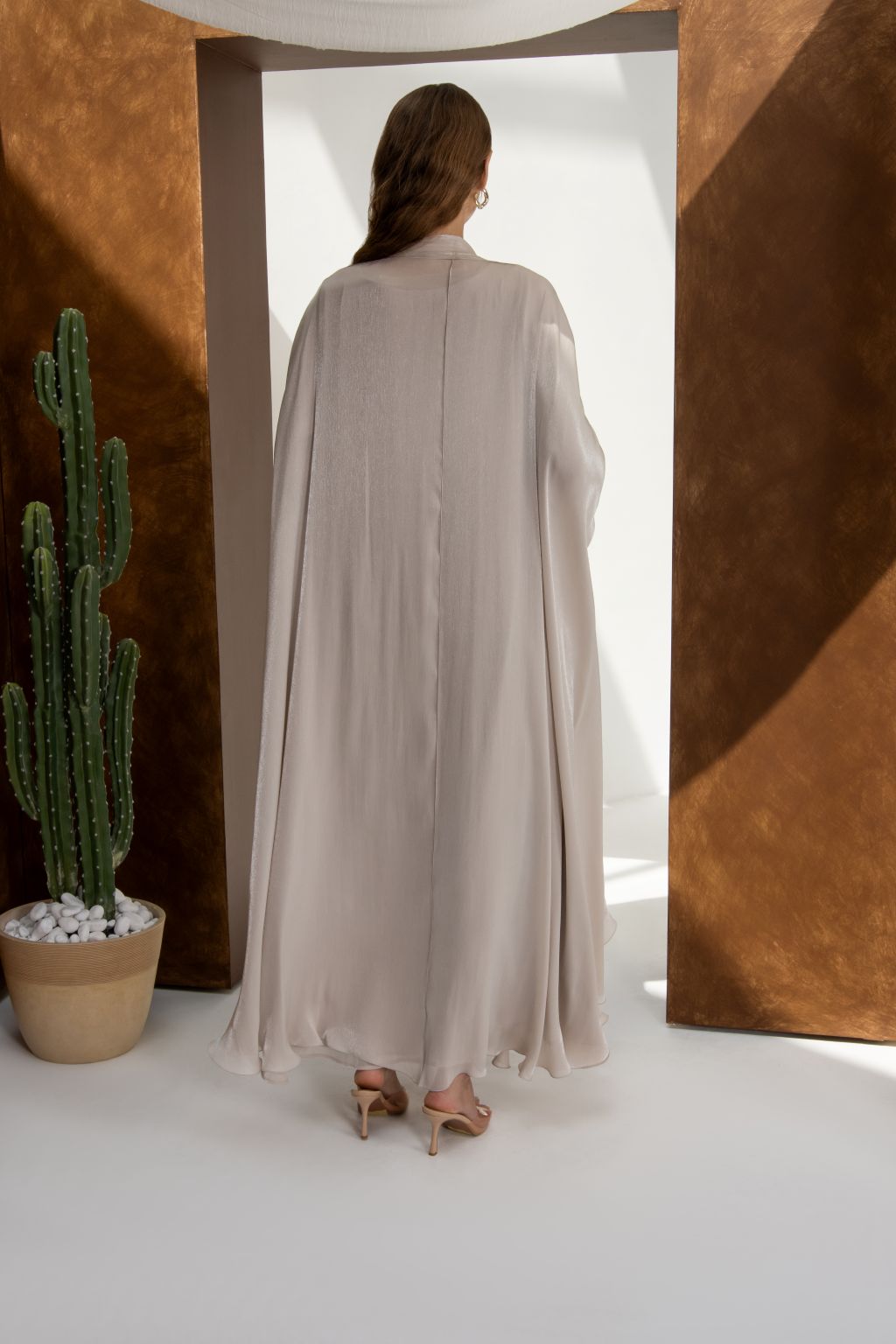 Back view of a woman wearing an elegant Swan Flow abaya by Selected Lines in a neutral tone with flowing fabric