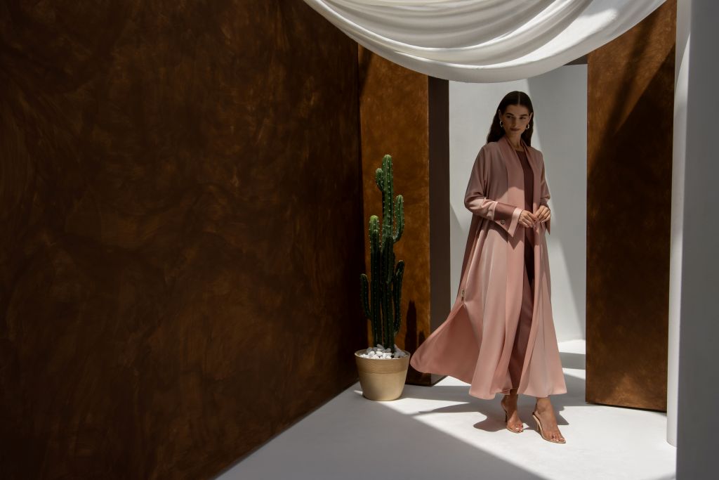 Woman wearing a high quality formal abaya by Selected Lines in soft pink standing near a cactus plant