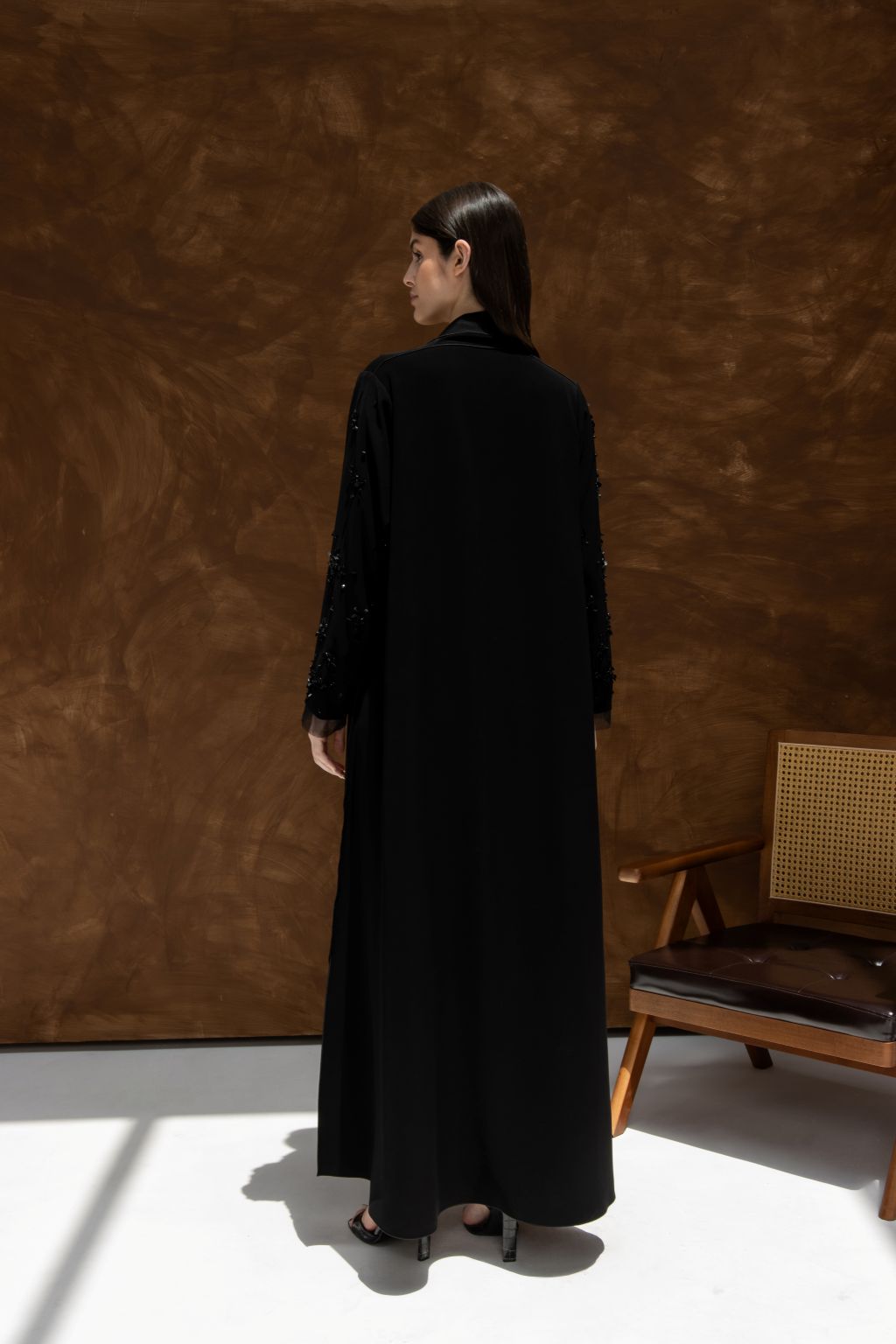 Selected Lines La Lueur abaya Set in black worn by model standing with back facing camera in minimalist room