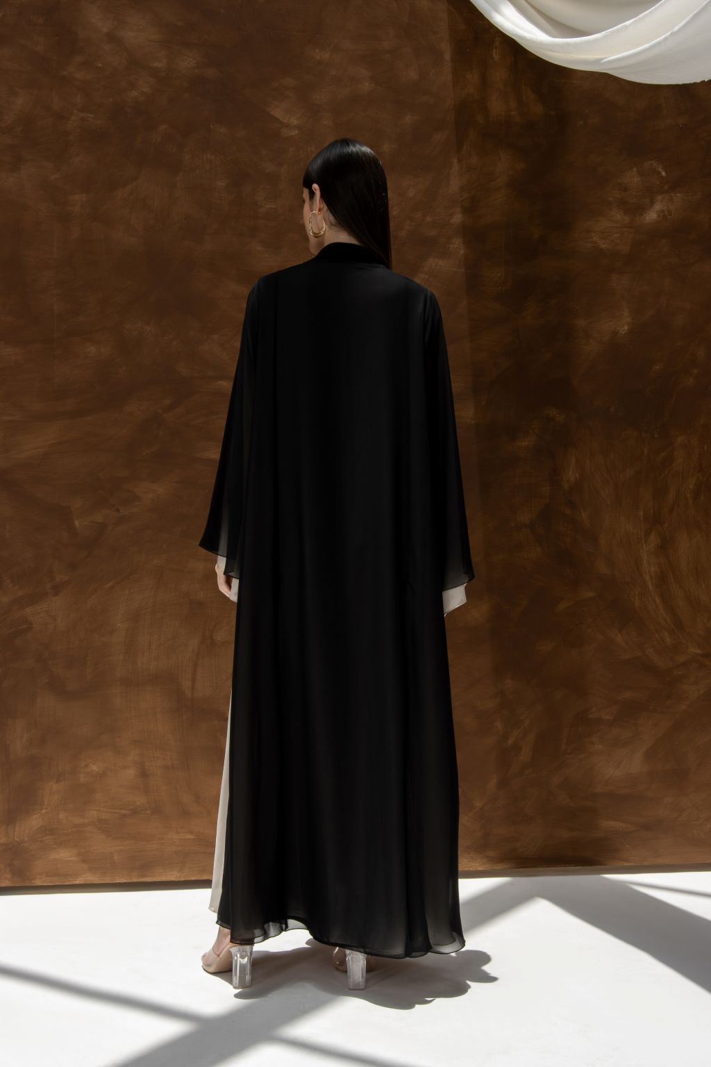 Back view of model wearing black Layered Grace Abaya by Selected Lines in a minimal studio setting