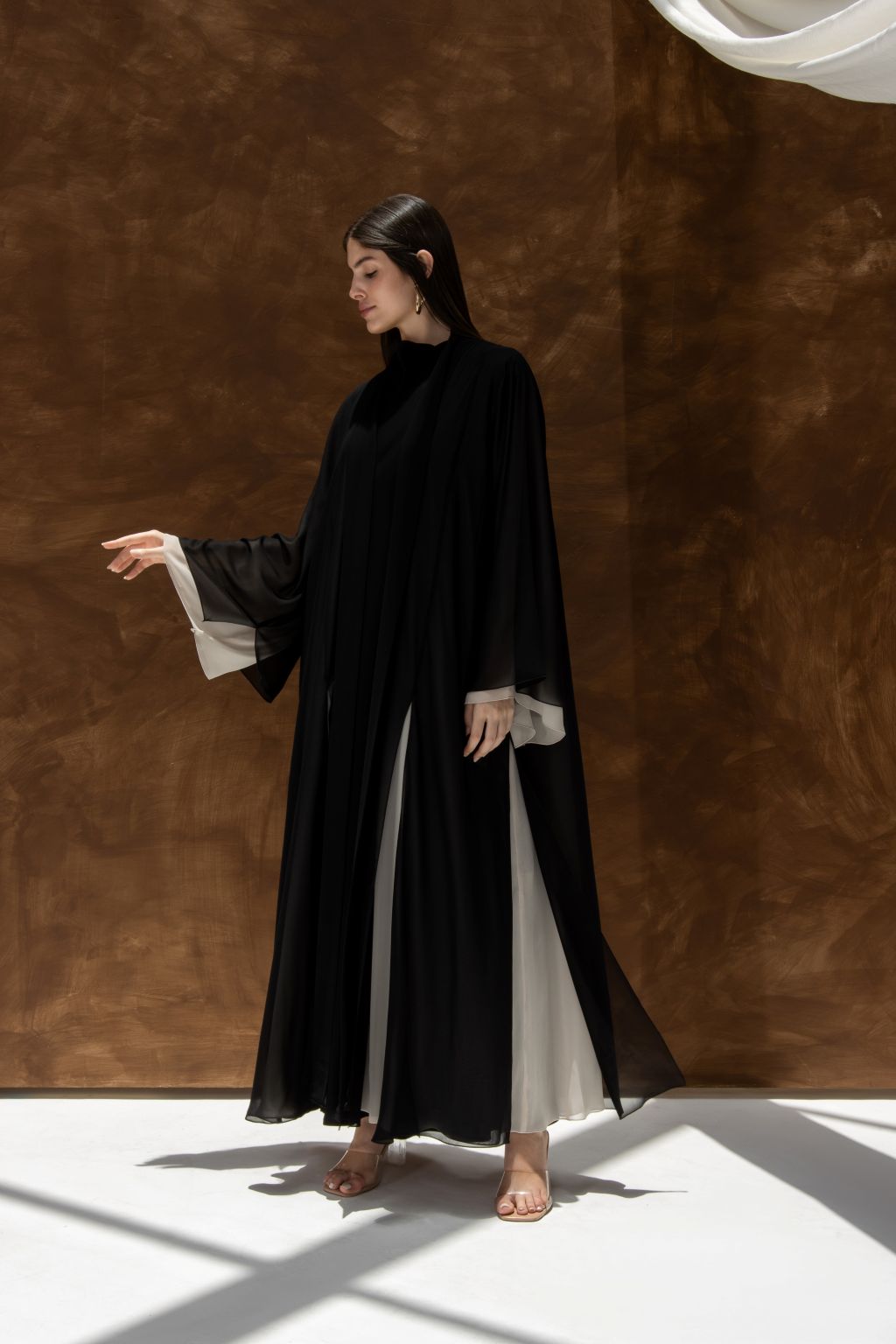 Selected Lines Layered Grace Abaya in black with white inner layers worn by woman standing against brown backdrop
