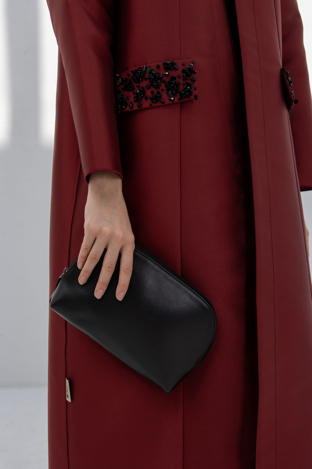 Luxury burgundy women's coat with beaded embellishments and a stylish black clutch bag