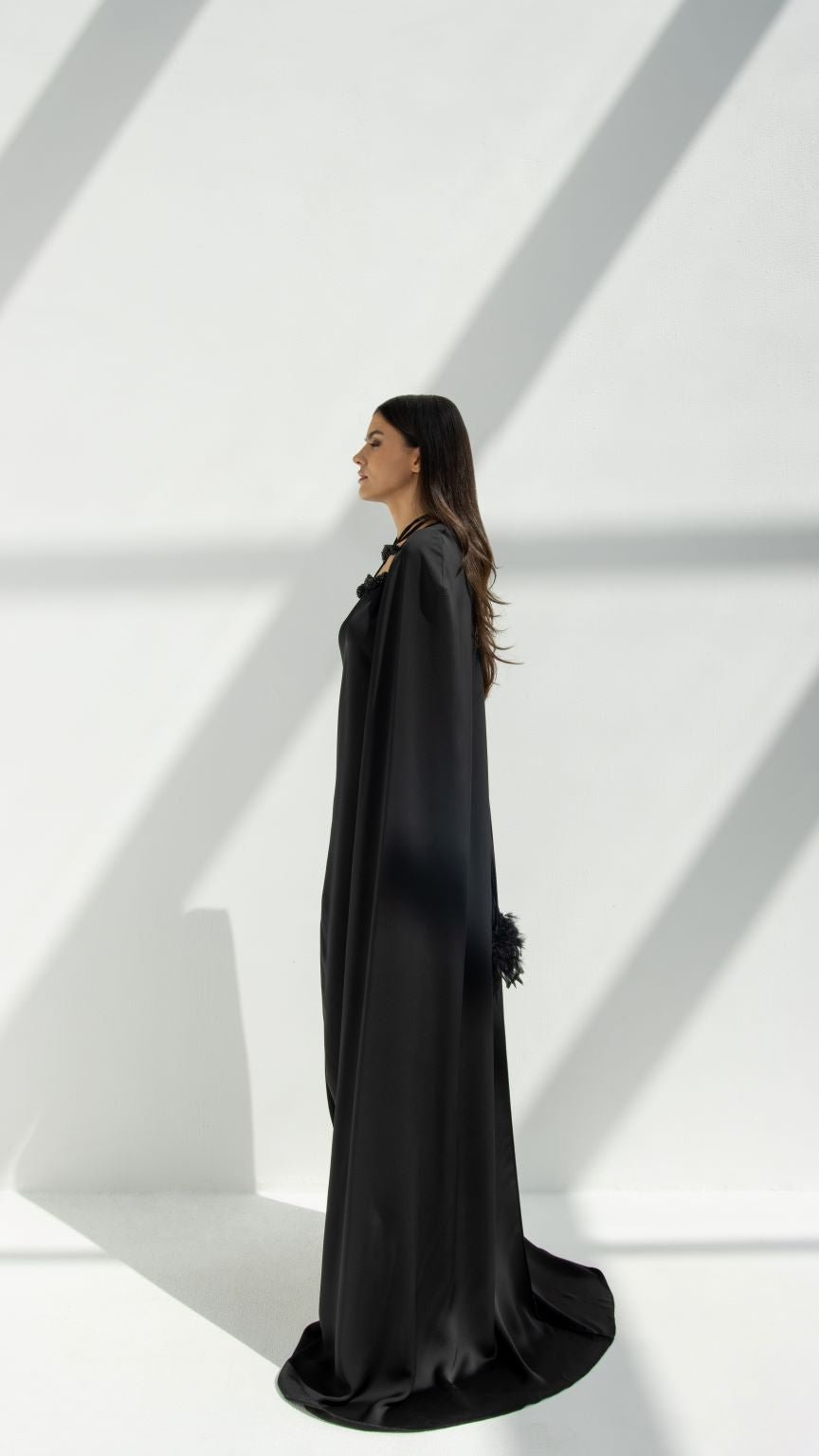 Elegant woman wearing a black luxury cape chain abaya by Selected Lines in a bright minimalist setting