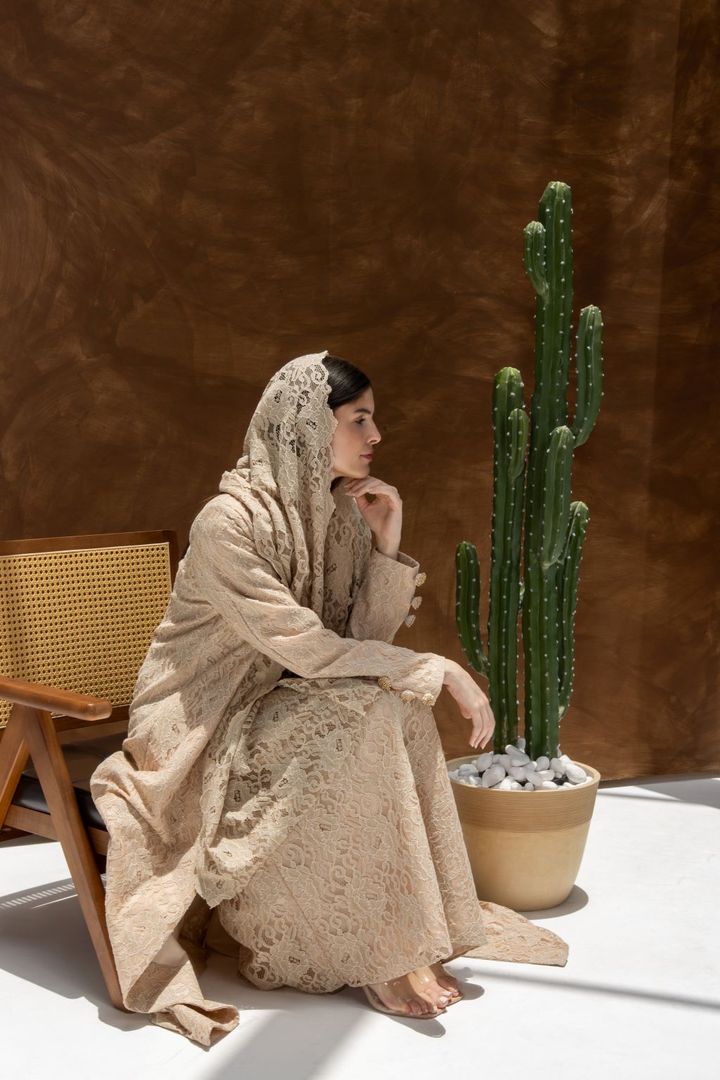 Selected Lines luxury lace Duntel Enchante' abaya worn by woman sitting on chair near cactus