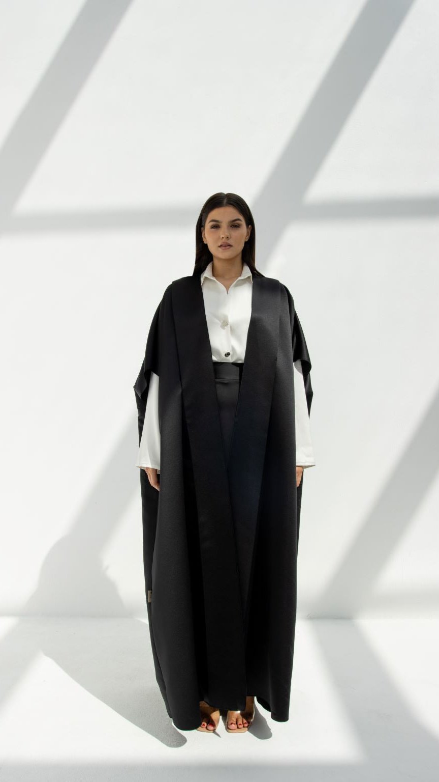 Selected Lines luxury yoga abaya in black worn over white shirt and pants with minimalist background