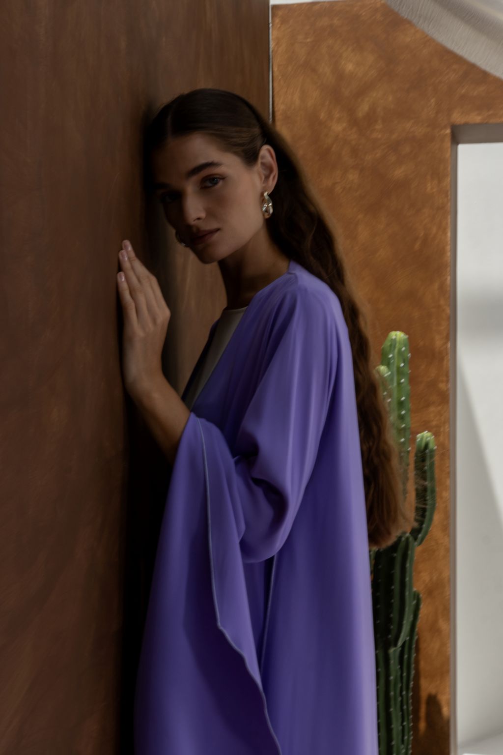 Woman wearing a purple Onz SLC Signature robe abaya by Selected Lines leaning against a brown wall