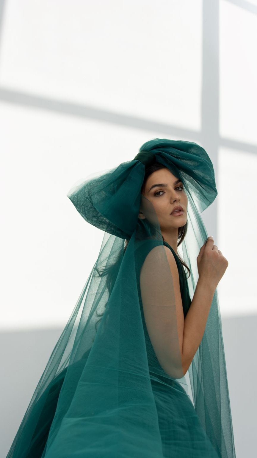 Elegant woman modeling a refined bow party dress with a large bow and sheer overlay in teal