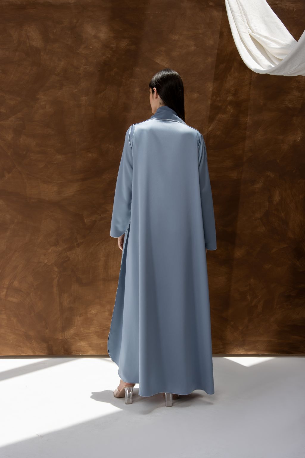 Selected Lines silhouette abaya with refined design in soft blue worn by model standing against brown background
