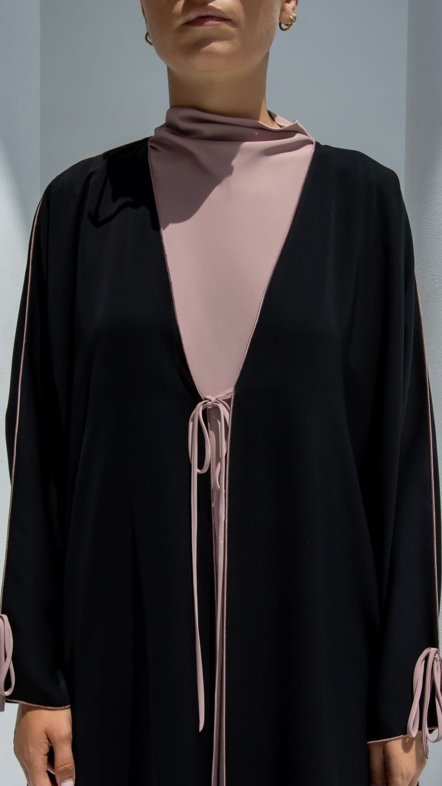 Elegant Bahraini ribbon abaya in black featuring a soft pink inner layer and stylish tie details