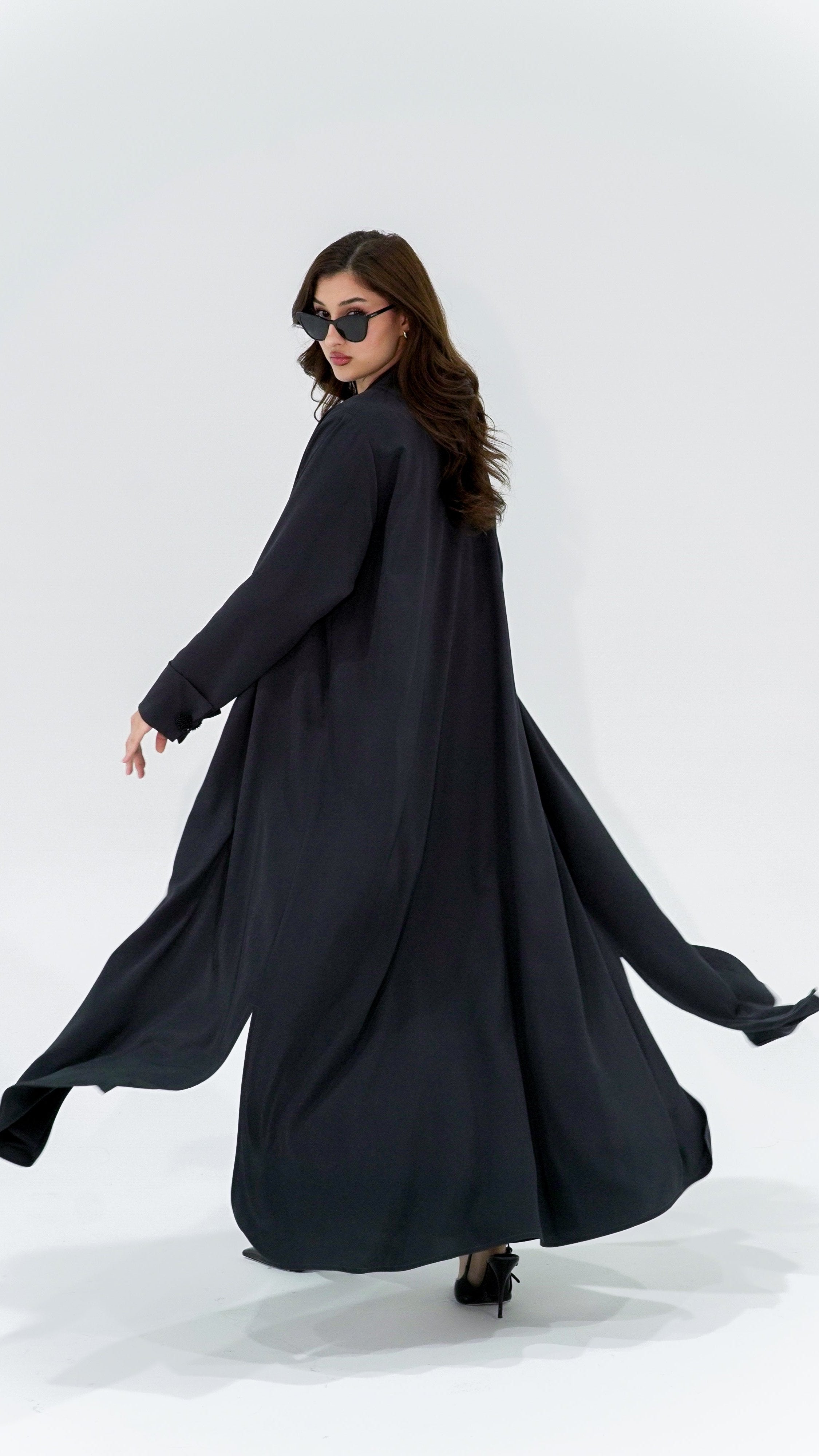 Woman wearing a flowing charcoal pearl sleeve abaya walking with sunglasses on