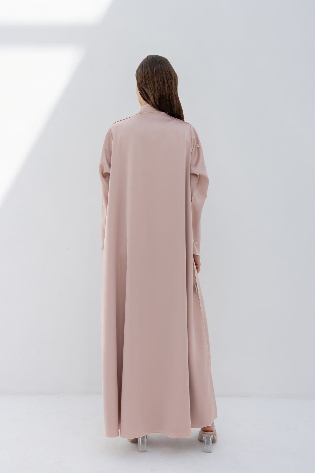 Back view of a woman wearing a blush pink luxury fashion abaya by Selected Lines in a minimalist setting