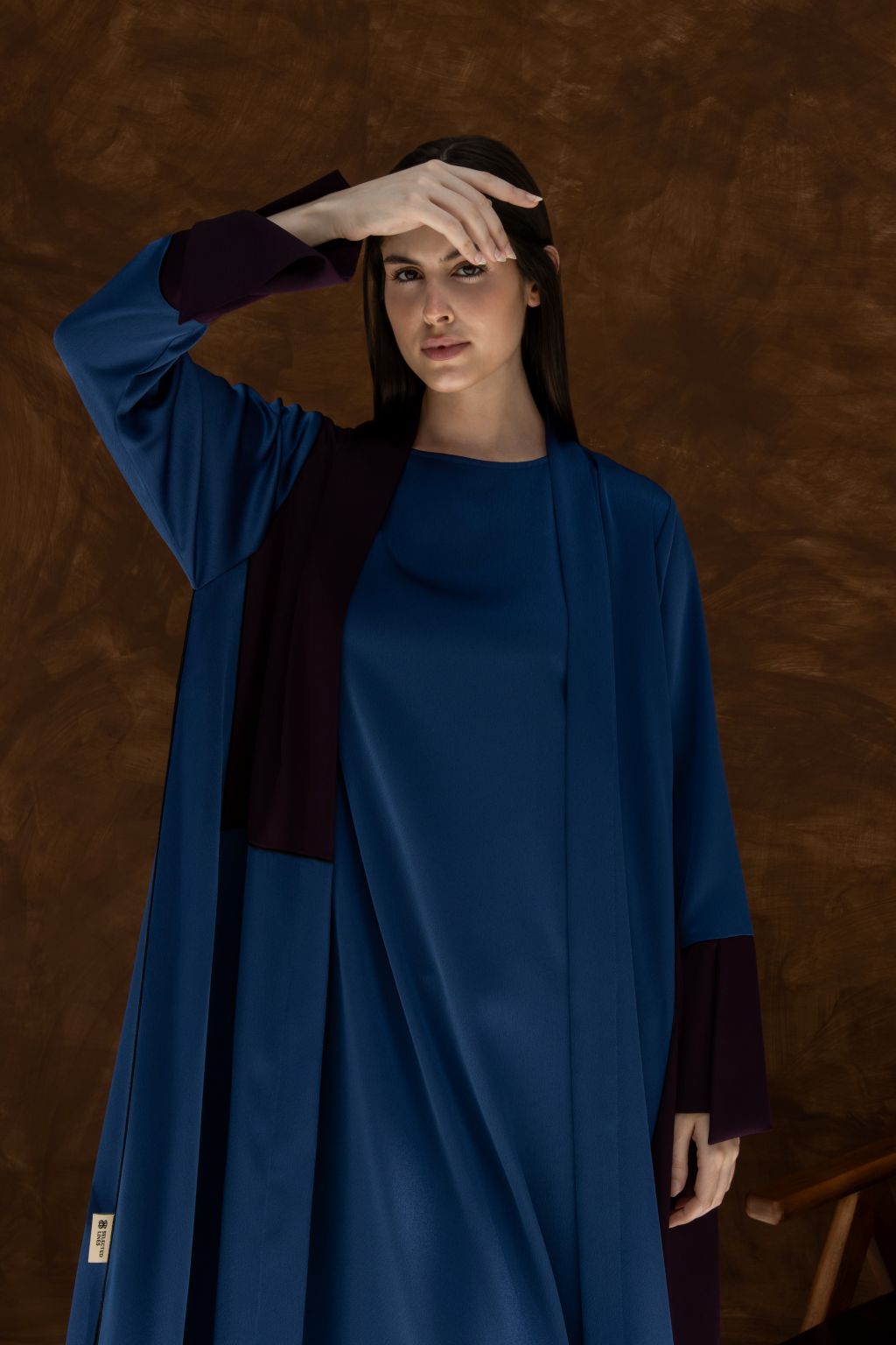 Selected Lines luxury HueLine blue abaya with dark sleeve accents worn by model on brown background