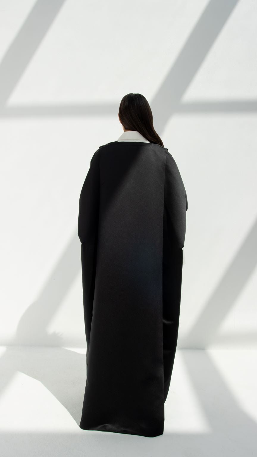 Back view of a woman wearing a black luxury yoga abaya by Selected Lines in bright natural light