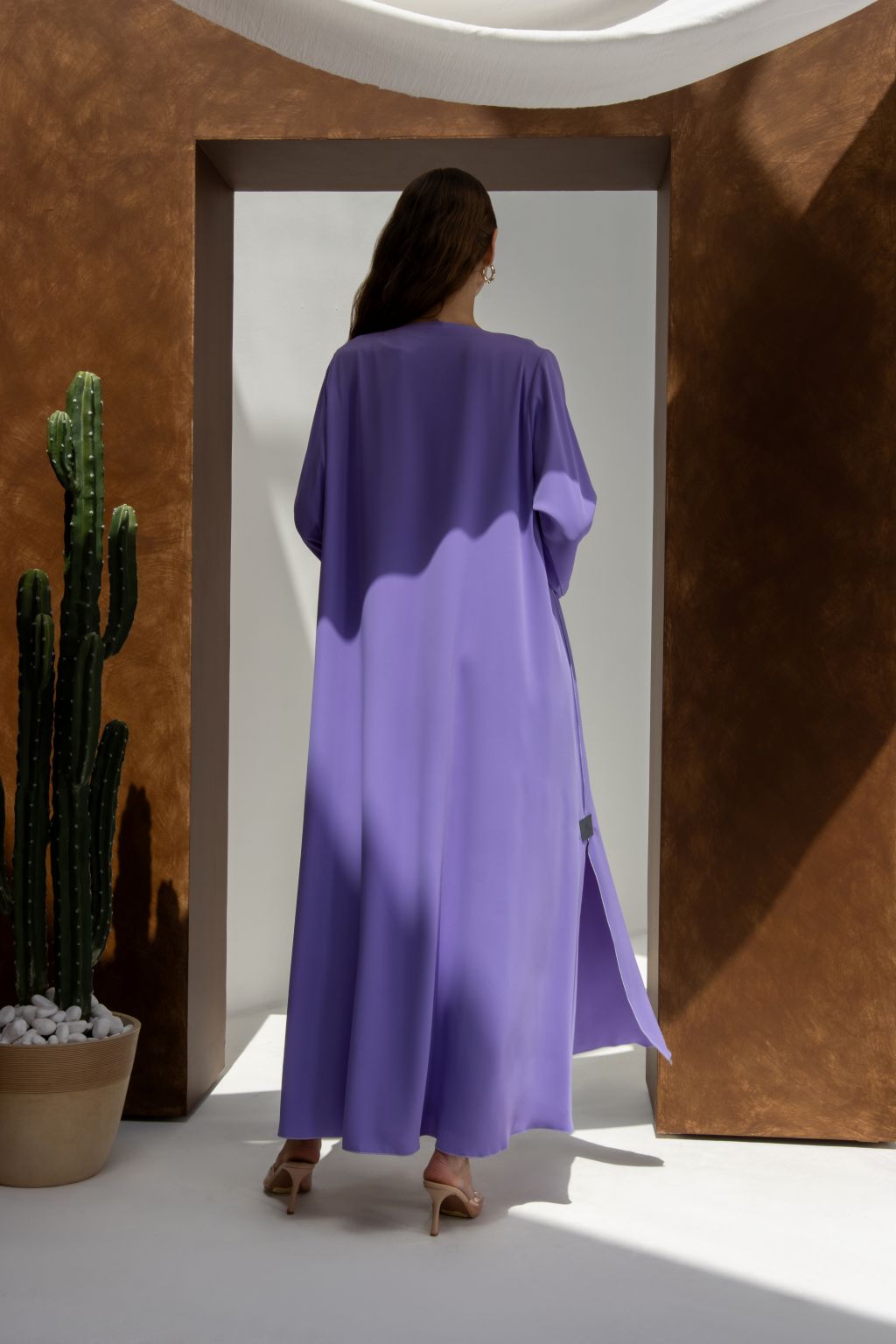 Back view of woman wearing purple Onz SLC Signature robe abaya standing near cactus and archway