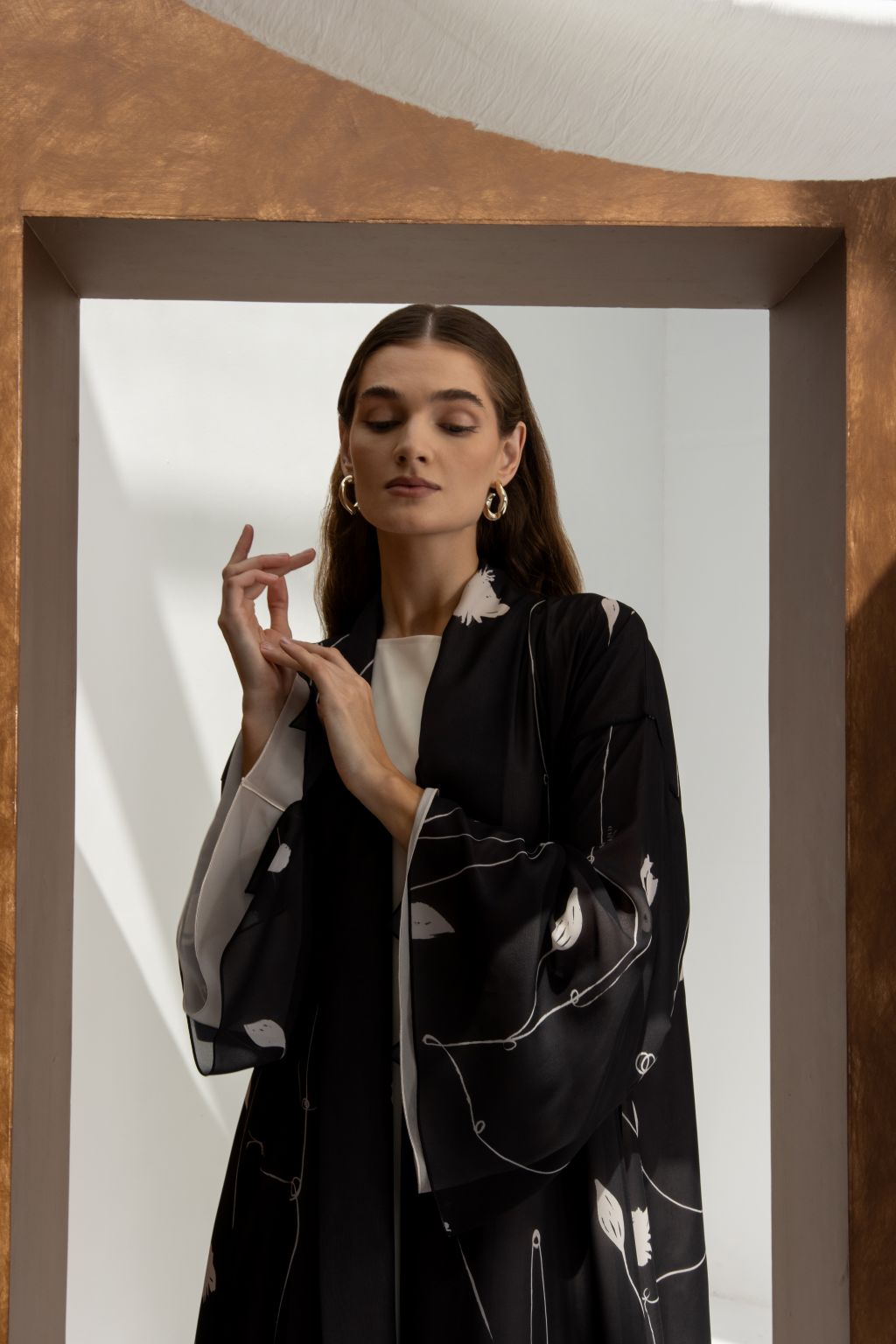 Selected Lines signature leaves black abaya with white leaf patterns worn by woman with gold hoop earrings