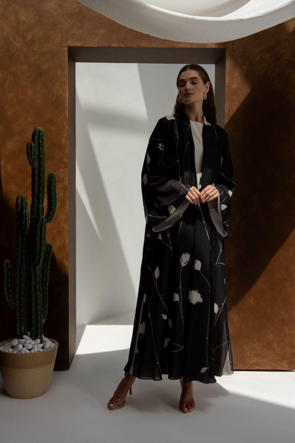 Selected Lines signature leaves black abaya worn by model in minimalist setting with potted cactus